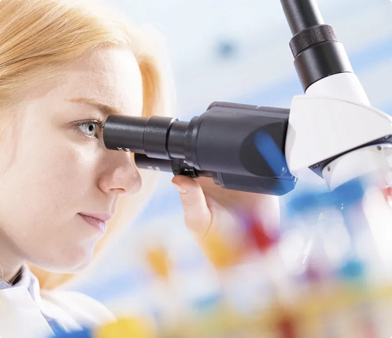 Scientist examining samples under microscope to ensure quality and innovation in pharma production