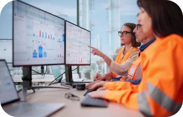 Operators in a control room monitor multiple screens showing process status and alarm indicators.