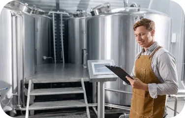 Technician reviewing production data on tablet in front of large industrial tanks.