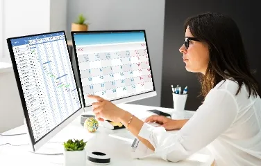 Businesswoman analyzing data on dual computer screens