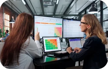Two colleagues analyzing data across multiple monitor screens