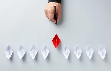 Leader guiding red paper boat among white ones symbolizing innovation