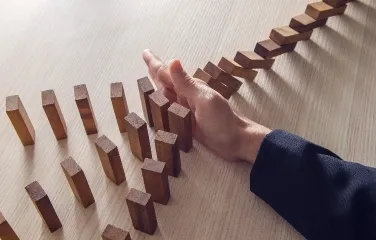Hand stopping falling dominoes symbolizing risk prevention