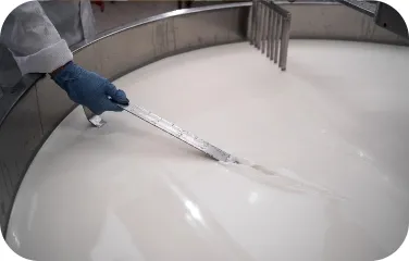 Worker stirring milk in a large stainless-steel vat.