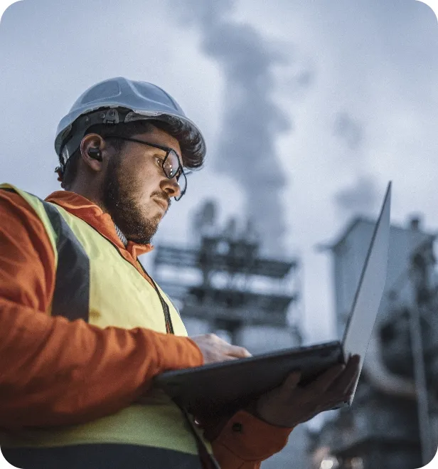 A field engineer in safety gear records and verifies process data on a laptop.