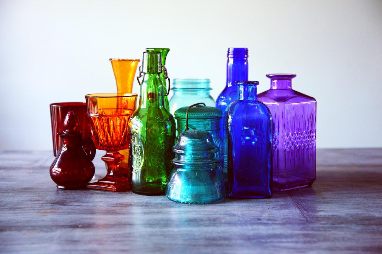 Collection of colorful glass bottles and jars arranged on a wooden surface in natural light