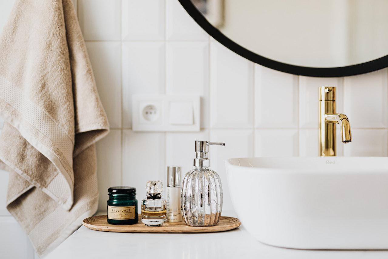 Modern bathroom sink with gold faucet, soap dispenser, perfume bottles, and a hanging beige towel