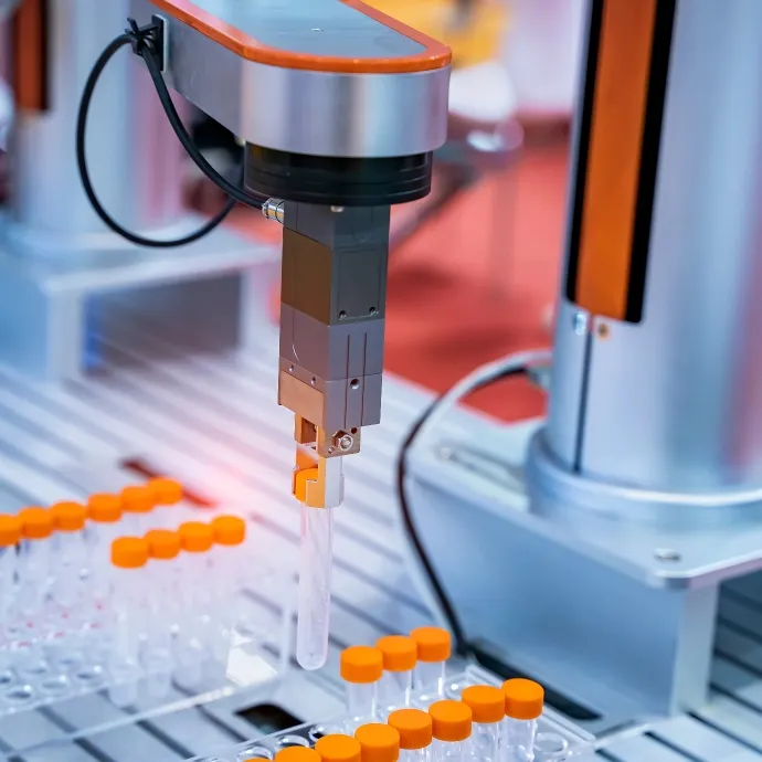 Robotic arm handling laboratory test tubes with orange caps on an automated machine platform