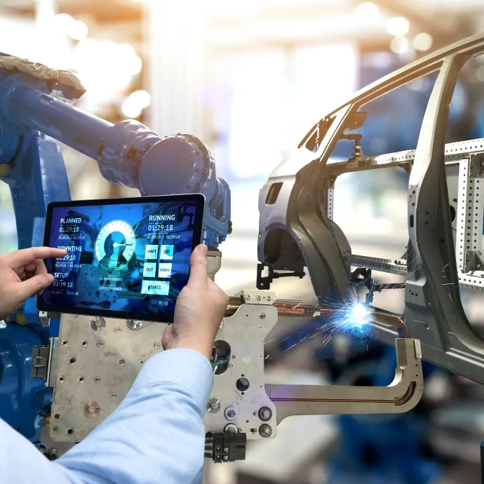 Engineer using a digital tablet to monitor smart factory robotics in automotive production